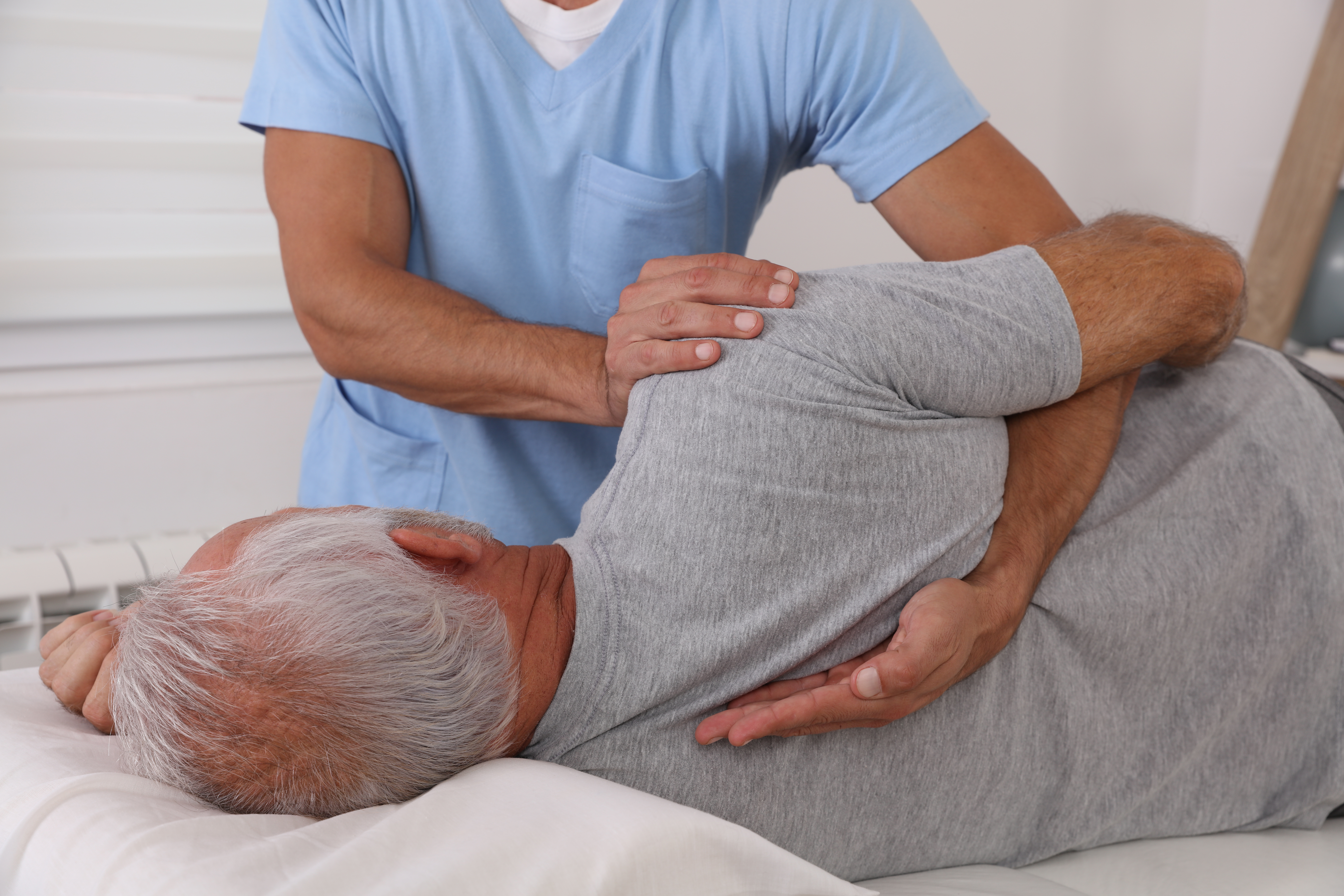 An older man lays on his side on an adjustment table while a chiropractor performs an adjustment.